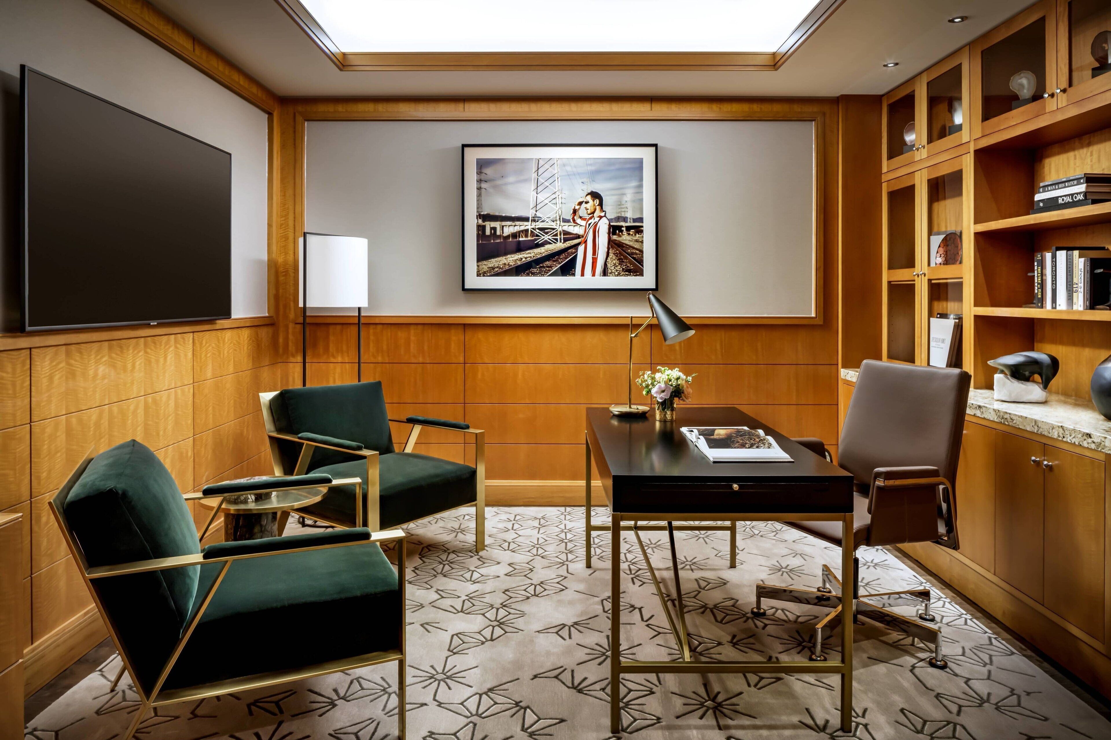 Une chambre d’hôtel moderne dotée d’un grand téléviseur à écran plat, d’un tableau représentant une femme dans un train, d’un bureau avec une lampe et d’une bibliothèque.