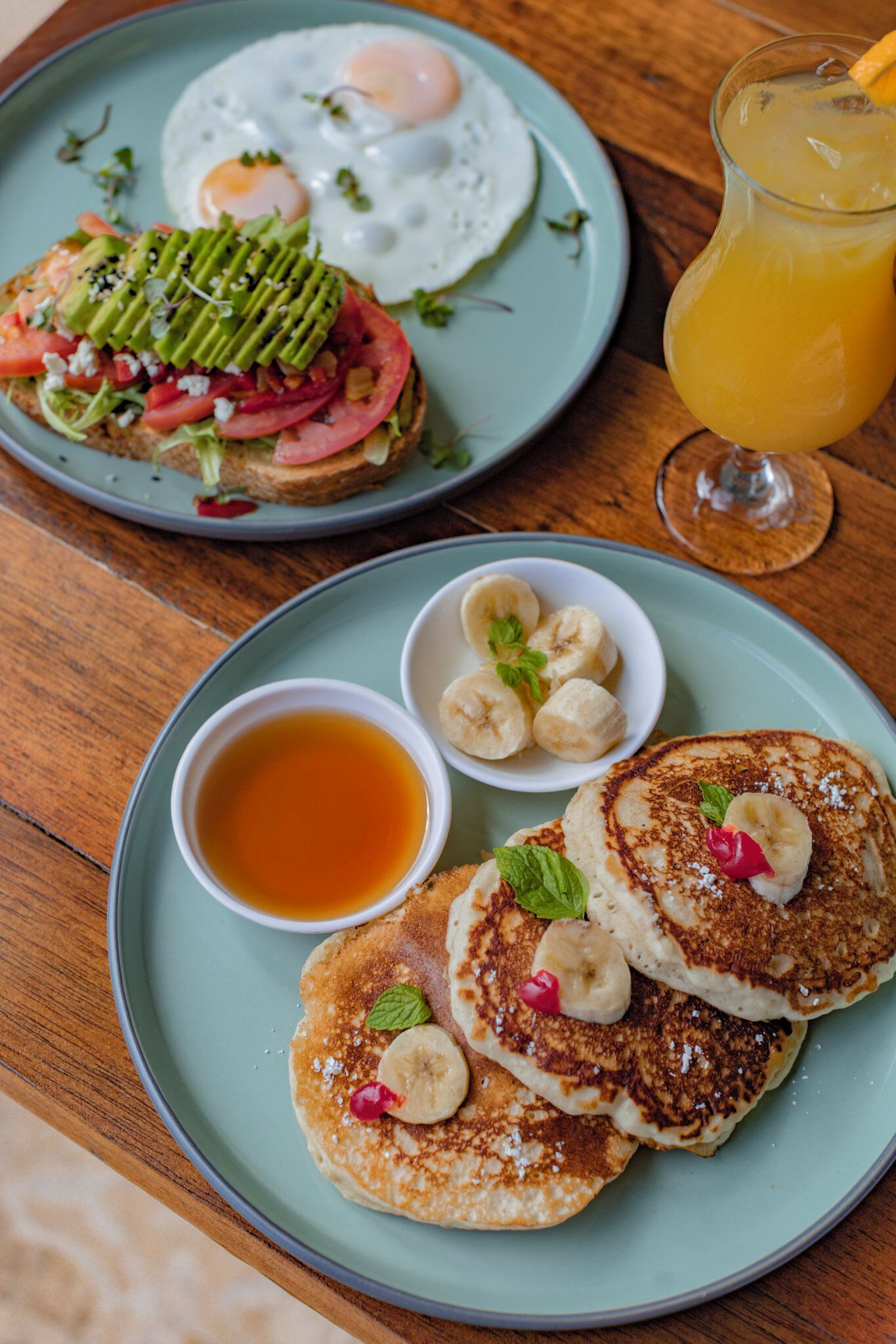 A breakfast plate with pancakes, a fried egg, avocado, tomato, and a glass of orange juice.