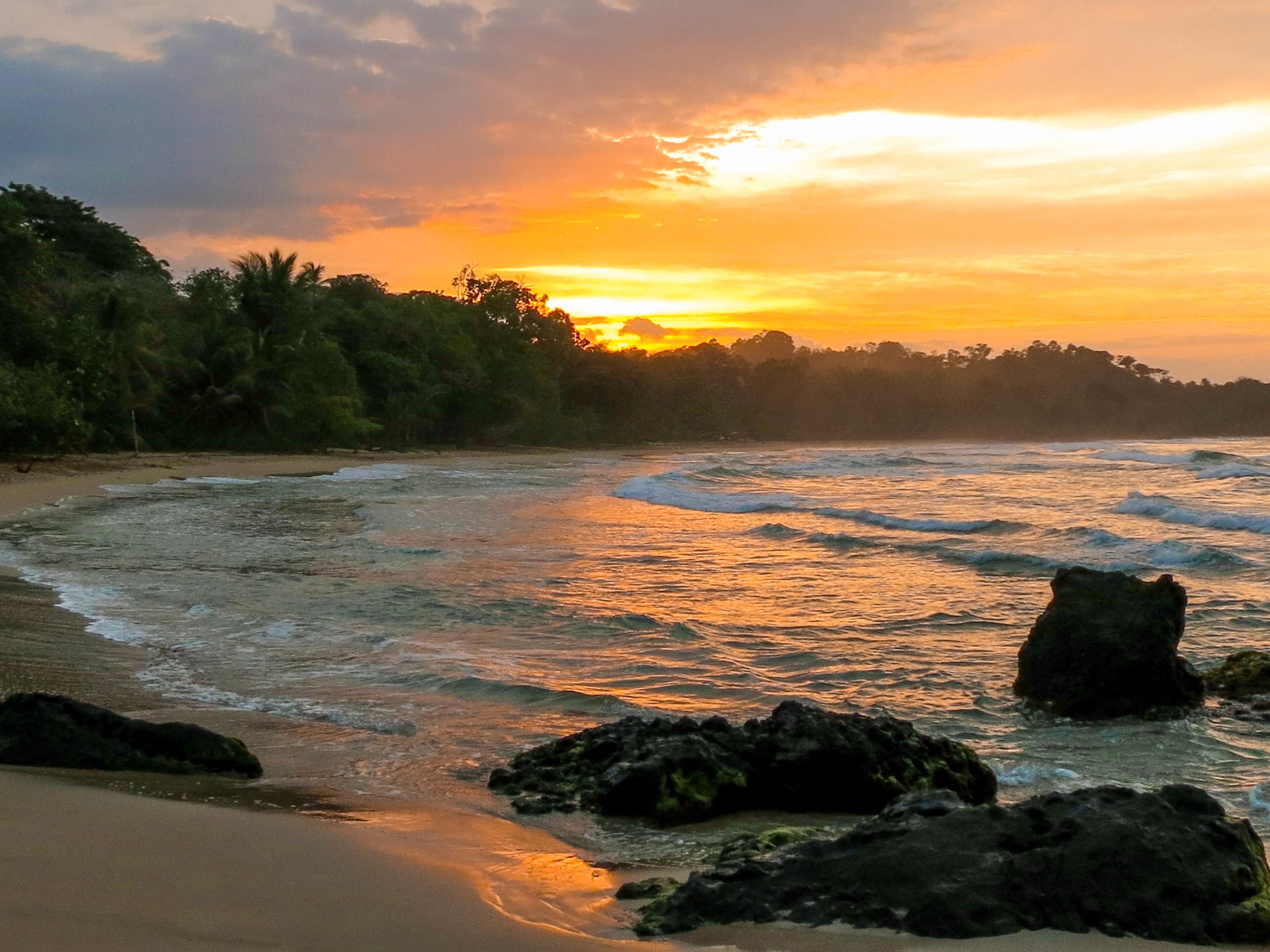 A beach with waves, rocks, and a sunset.