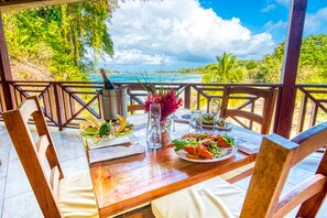 A wooden table set for two with a view of the ocean, a drink, and a plate of food. - Red Frog Beach Island Resort (Bastimentos)