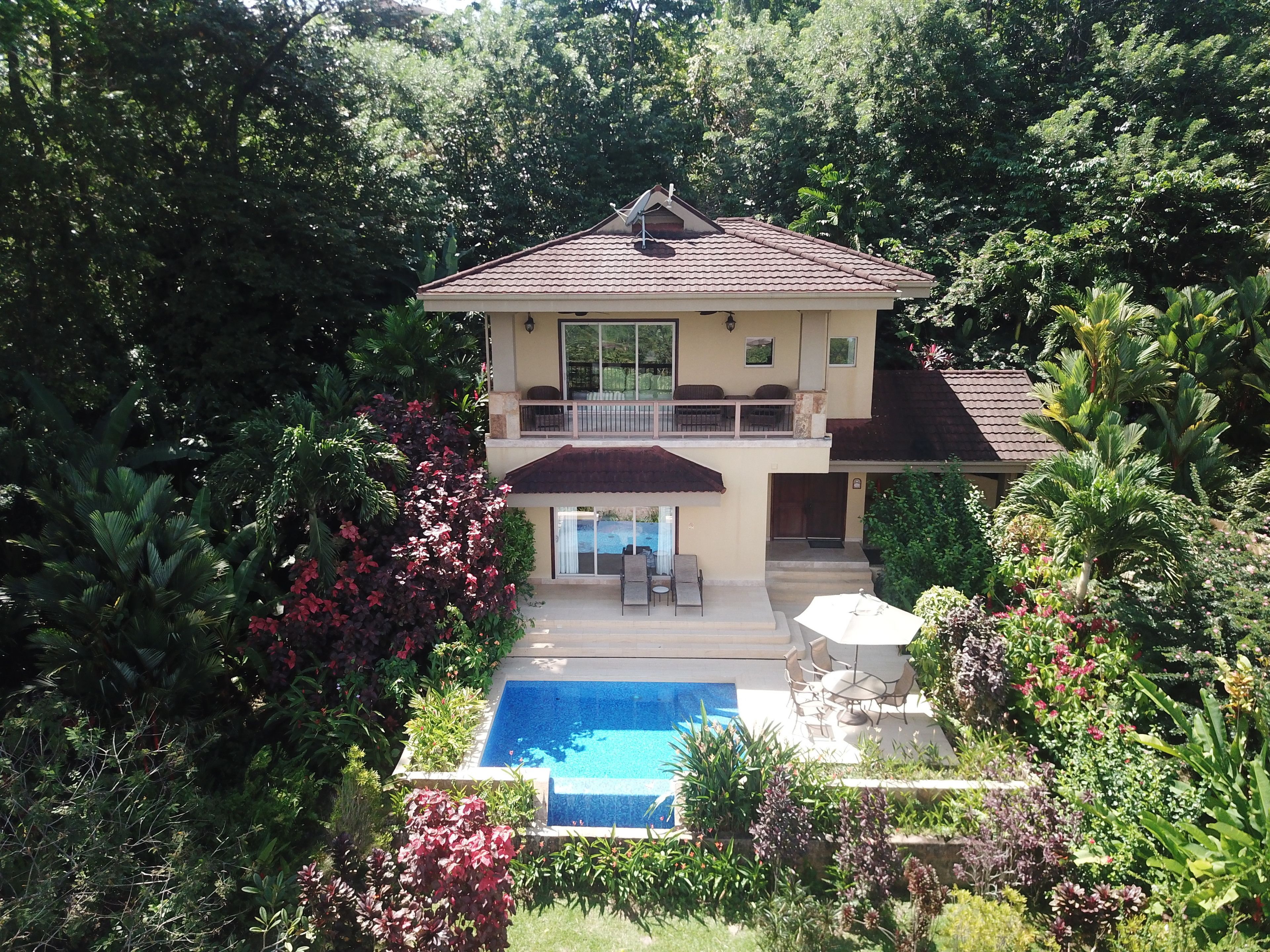 A two-story house with a swimming pool, surrounded by lush greenery.
