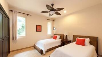 Una habitación de hotel con dos camas, ventilador de techo y ventana con cortinas.