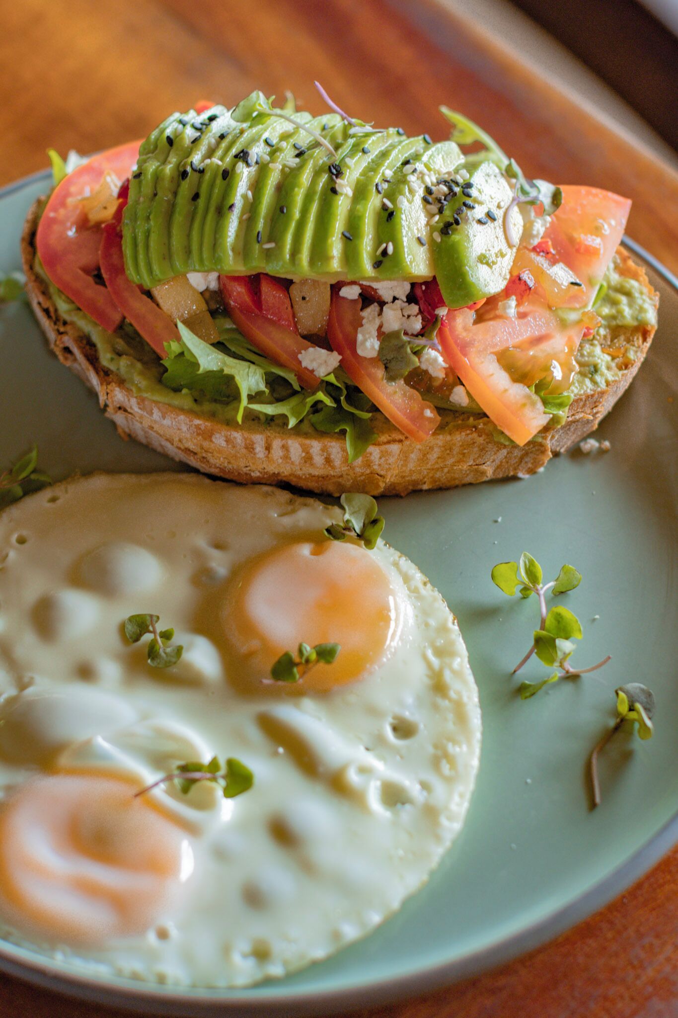 A sandwich with avocado, tomato, and greens on a plate with two sunny-side-up eggs.