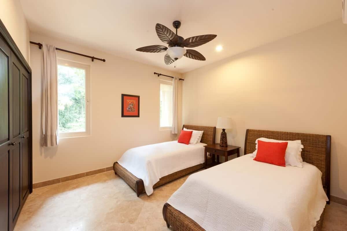 Une chambre avec deux lits, un ventilateur de plafond, une fenêtre et une porte.