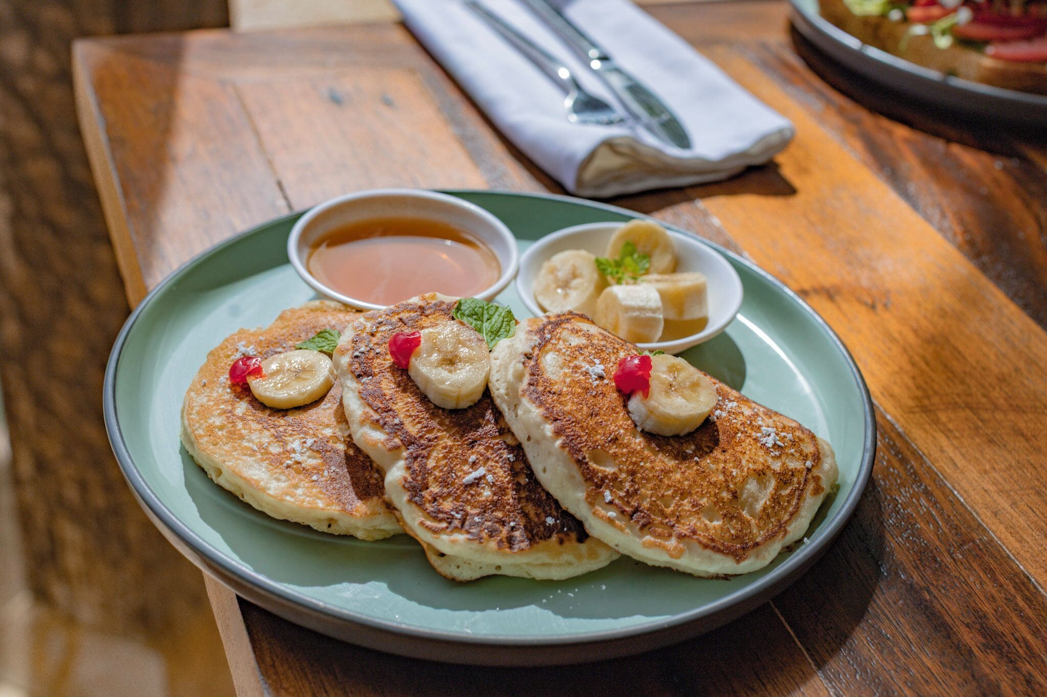 A plate of pancakes with bananas and a small bowl of syrup.