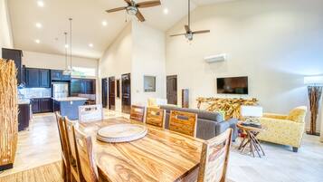 A spacious living area with a wooden dining table, a sofa, and a TV mounted on the wall.
