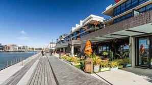 Eine Uferpromenade mit Holzsteg, Außenbereichen zum Sitzen mit Pflanzen und modernen Gebäuden mit Balkonen mit Blick auf das Wasser.