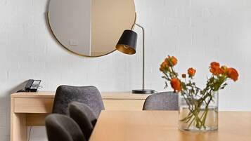 A modern office space with a round mirror, a desk with a telephone, two chairs, and a vase with flowers.