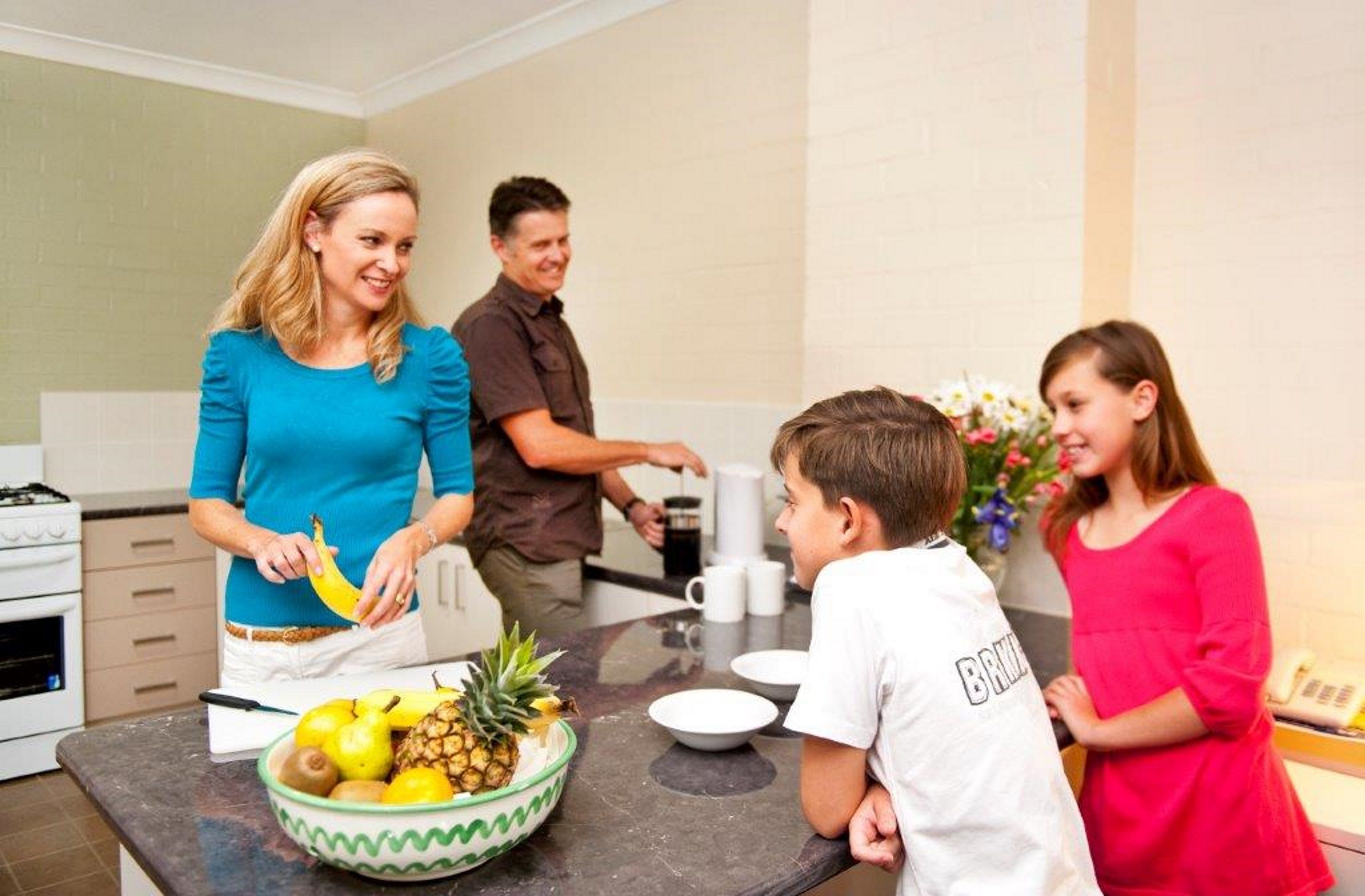A family in a modern kitchen with a fruit bowl on the counter, a stove, and a sink.