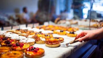 Diverse gebakjes in etalage, waaronder vruchten-toegesneden taartjes en desserts, terwijl een hand er een pakt.