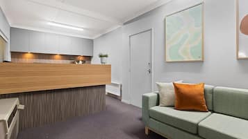 Een moderne receptiebalie met een houten toonbank, een groene bank met een bruin kussen en een lijst met een abstract schilderij aan de muur.