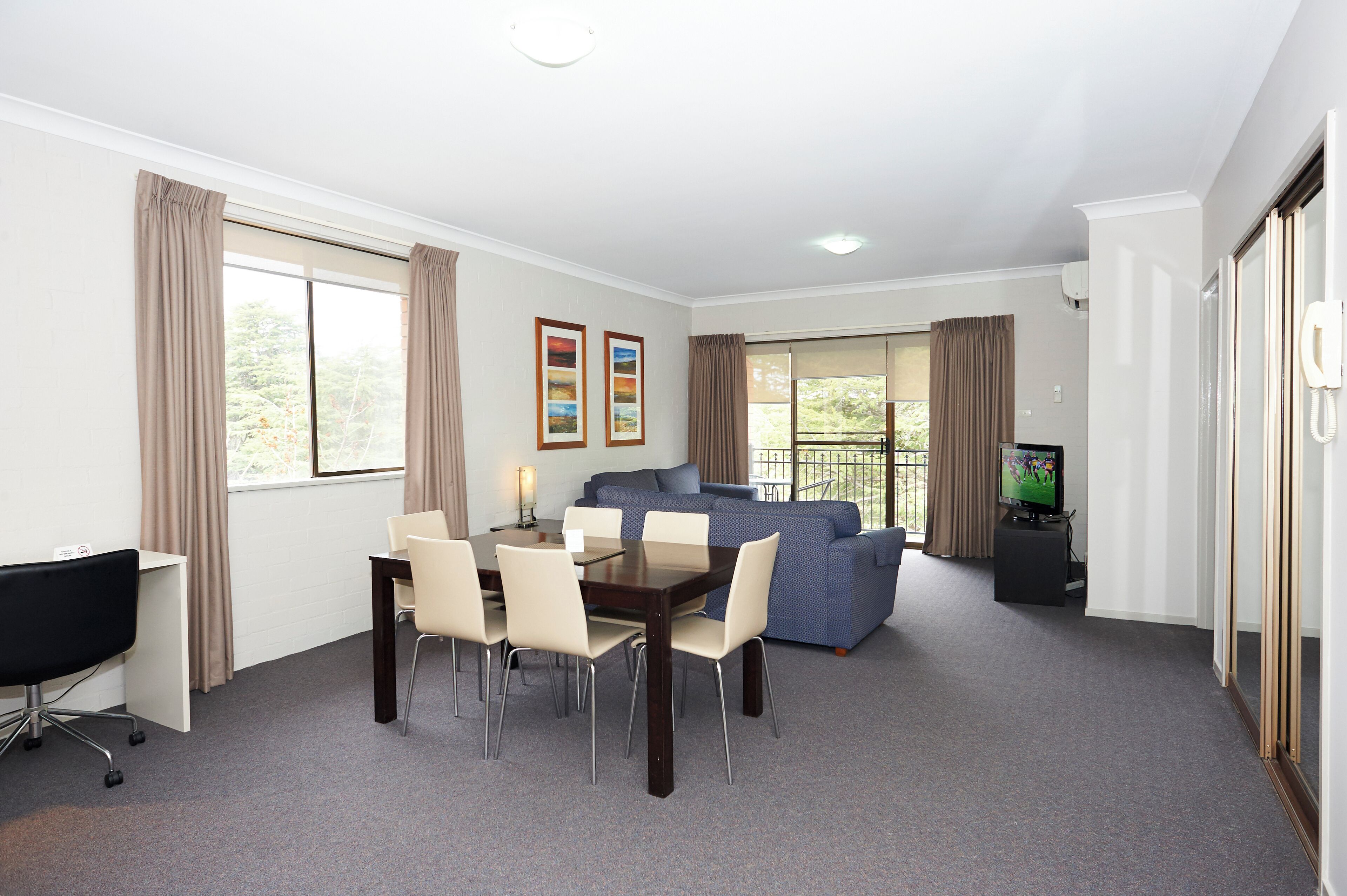 A room with a dining table, chairs, a sofa, a TV, and a desk.