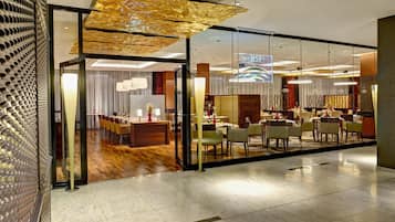 A modern hotel lobby with a glass partition, a reception desk, and a dining area with tables and chairs.