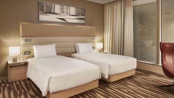 A hotel room with two beds, a large window with curtains, a wall-mounted TV, and a patterned carpet.
