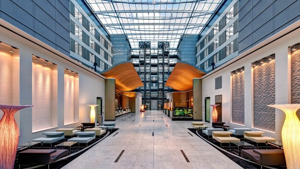 A spacious atrium with a high ceiling and glass panels, featuring seating areas and modern lighting fixtures. - Hilton Frankfurt Airport (Frankfurt)