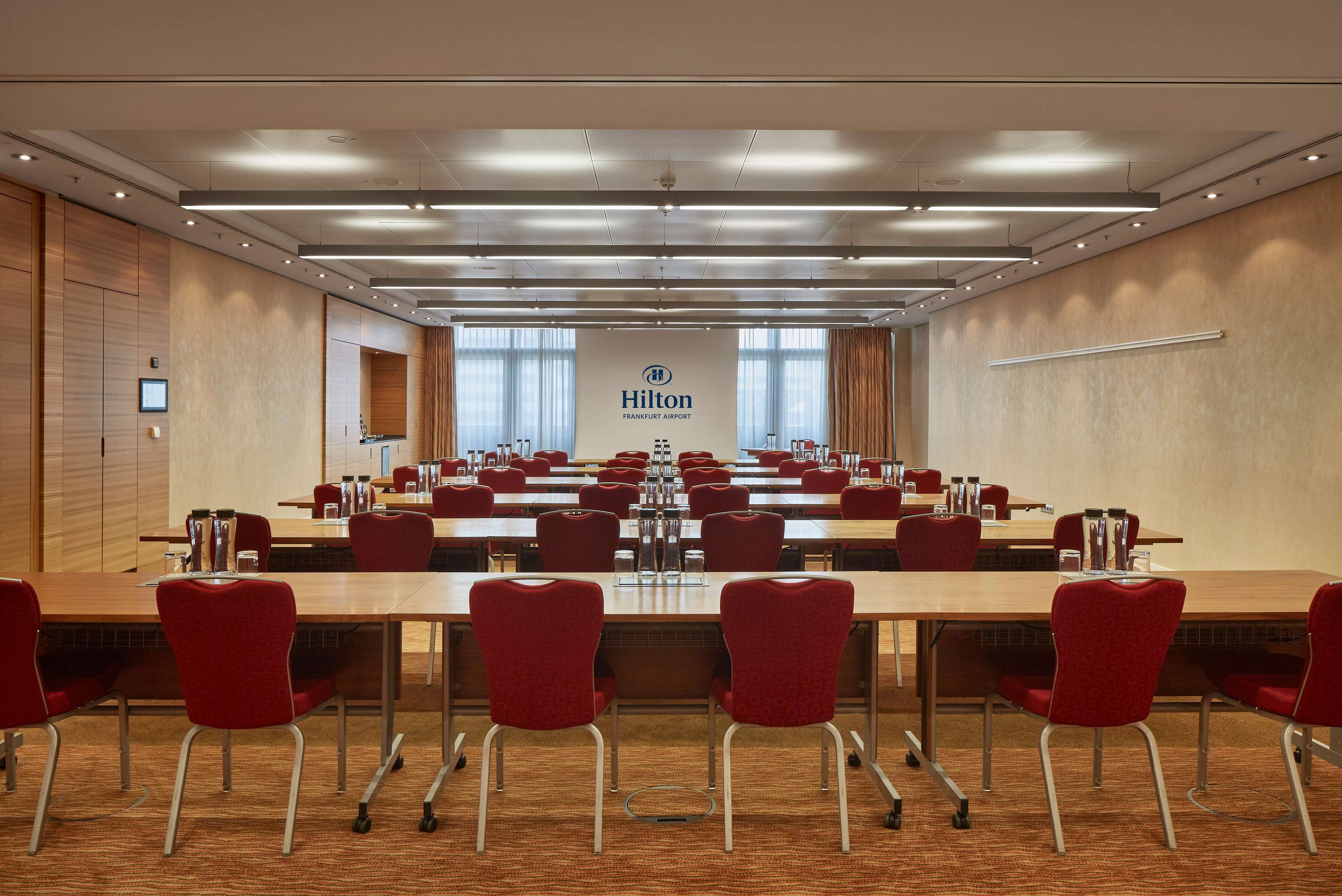 A large conference room with a long table, red chairs, and a sign for Hilton Frankfurt Airport.