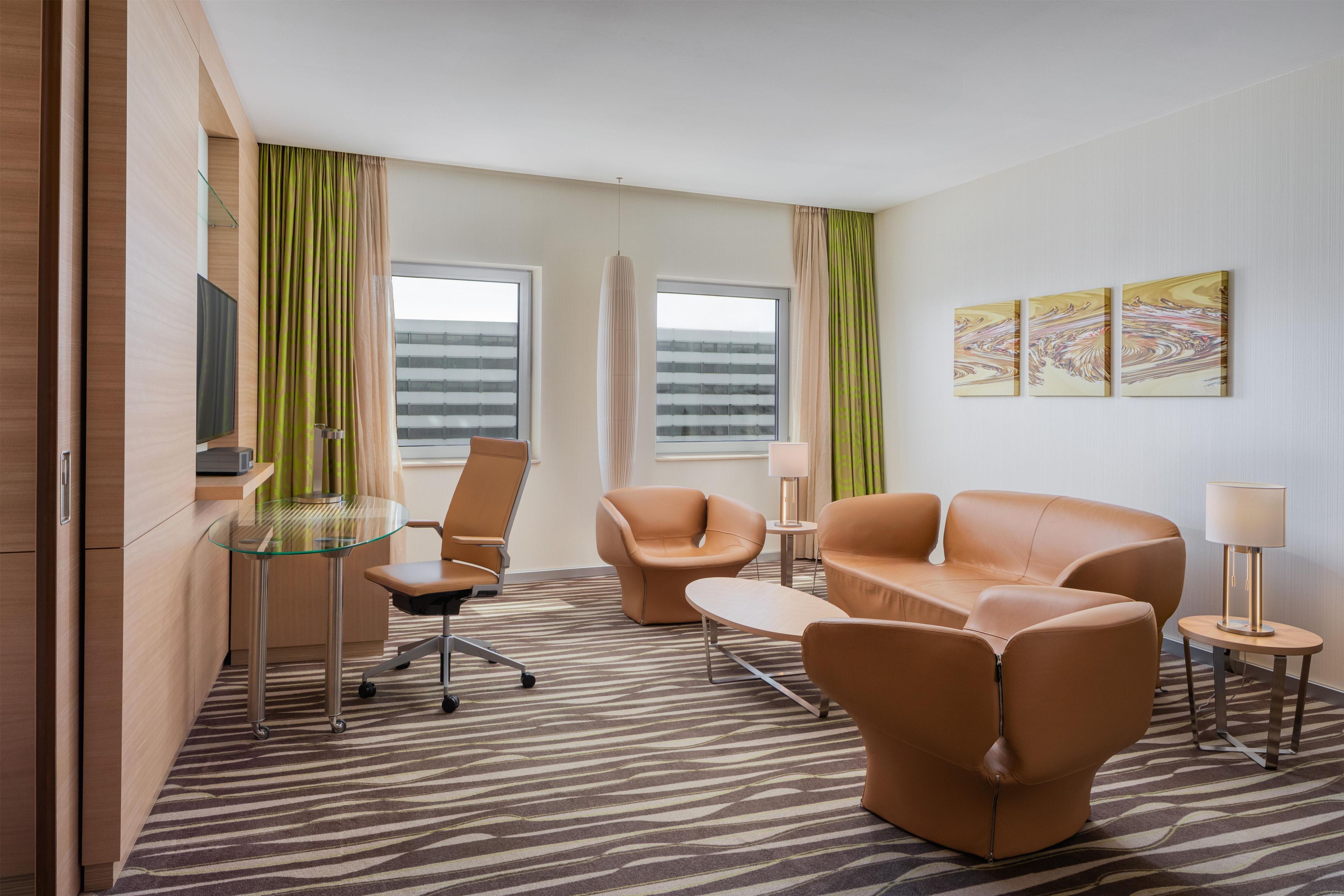 A hotel room with a sofa, chairs, a glass table, and a TV.