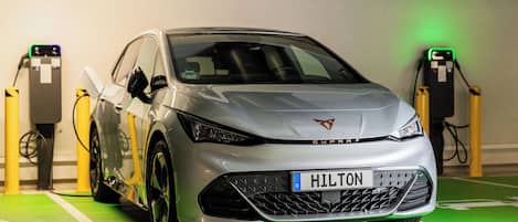 A silver car parked in a charging station with a green floor marking.