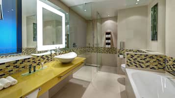 Un baño moderno con ducha envuelta en vidrio, un espejo grande y un tocador amarillo con lavabo blanco.
