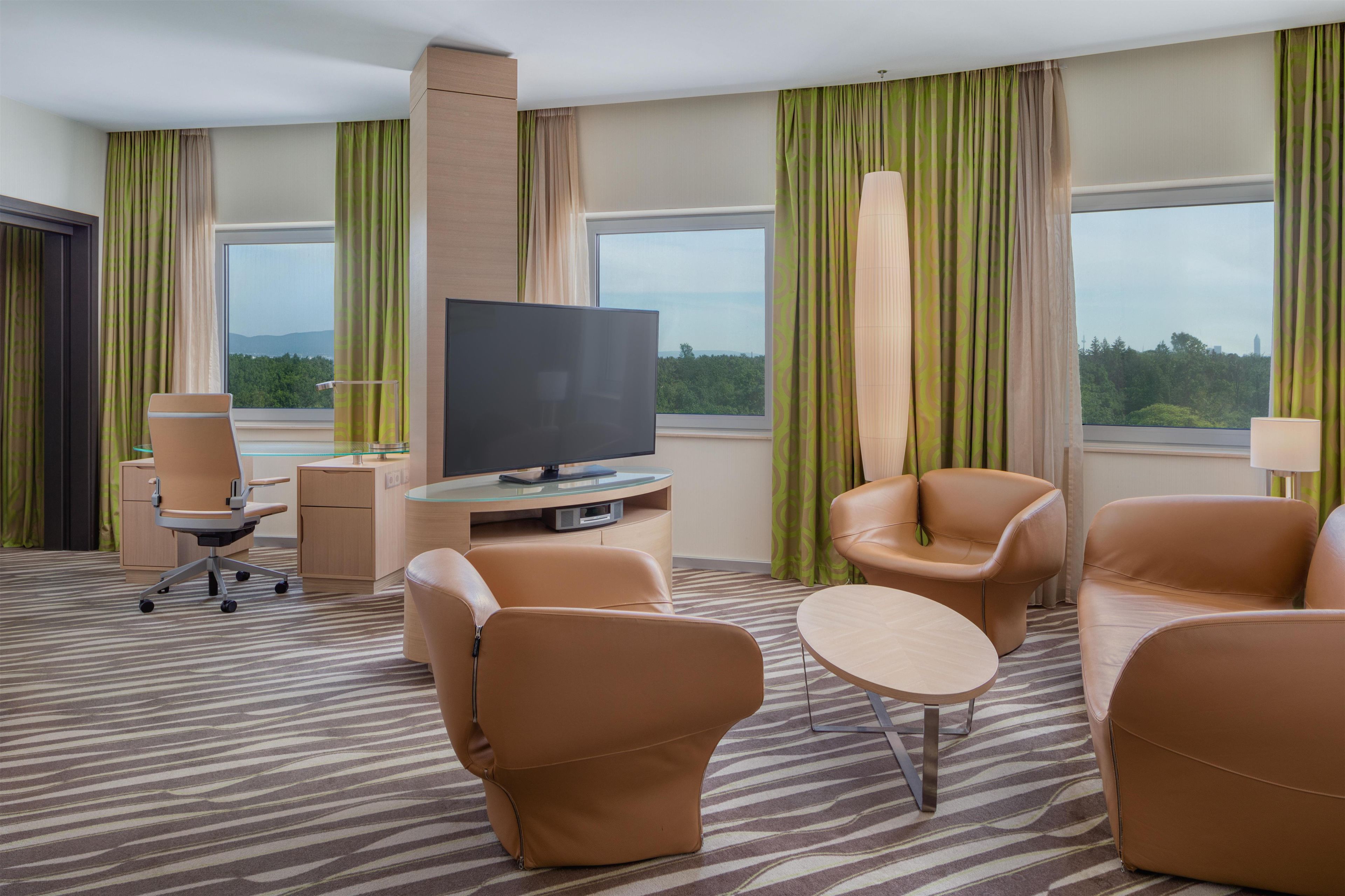 Ein Hotelzimmer mit Flachbildfernseher, Ledersesseln, einem kleinen runden Tisch und einem Glastisch.