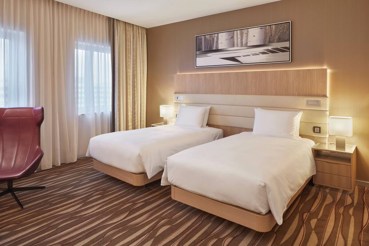 A hotel room with two beds, a red chair, and a large window with curtains.