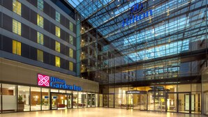 A modern hotel interior with a glass facade, multiple floors, and a prominent Hilton Garden Inn sign. - Hilton Frankfurt Airport (Frankfurt)