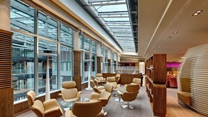 A modern interior with large windows, a high ceiling, and a seating area with tables and chairs. - Hilton Frankfurt Airport (Frankfurt)