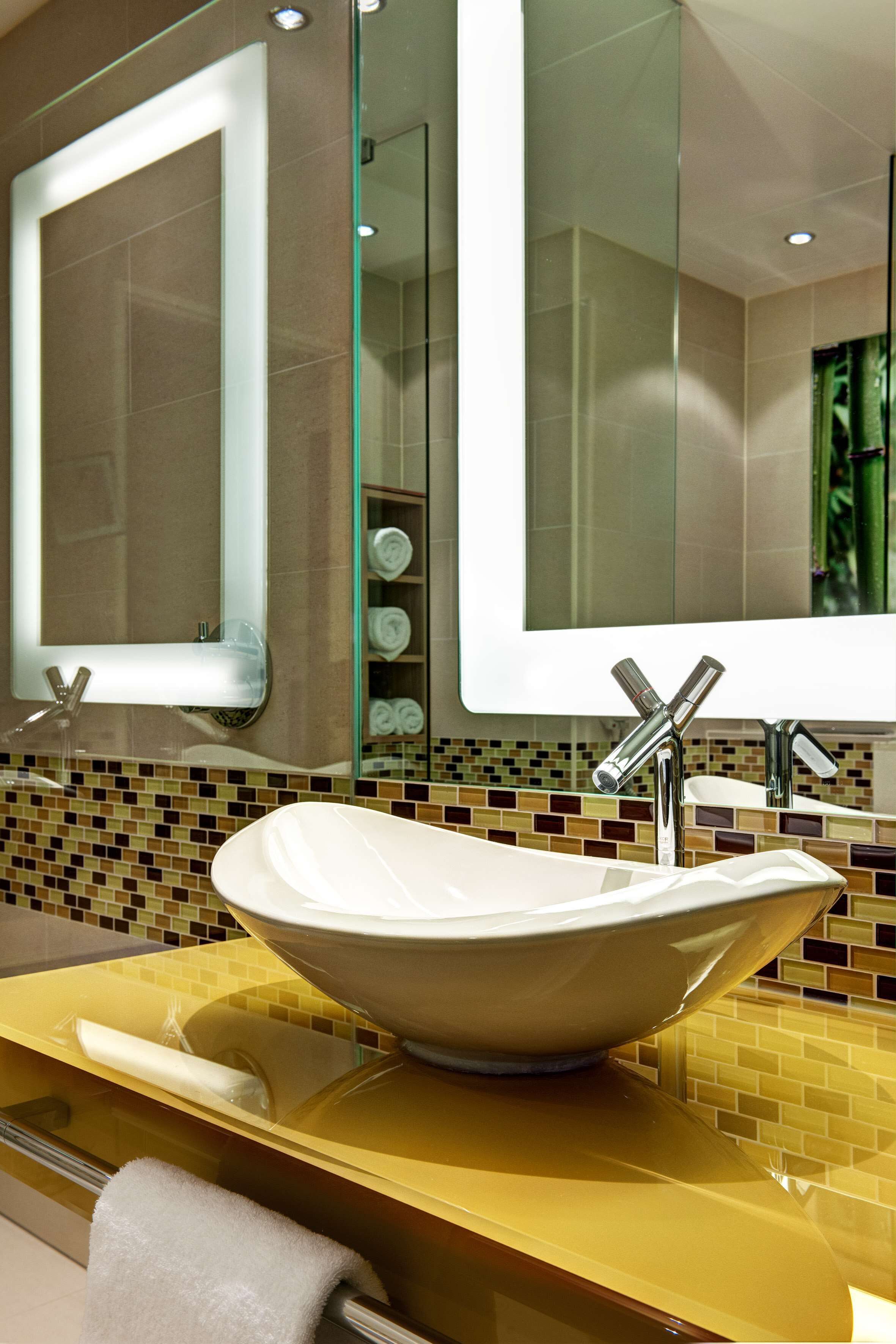 Un baño moderno con un espejo grande, un lavabo sobre encimera y un salpicadero de azulejos.