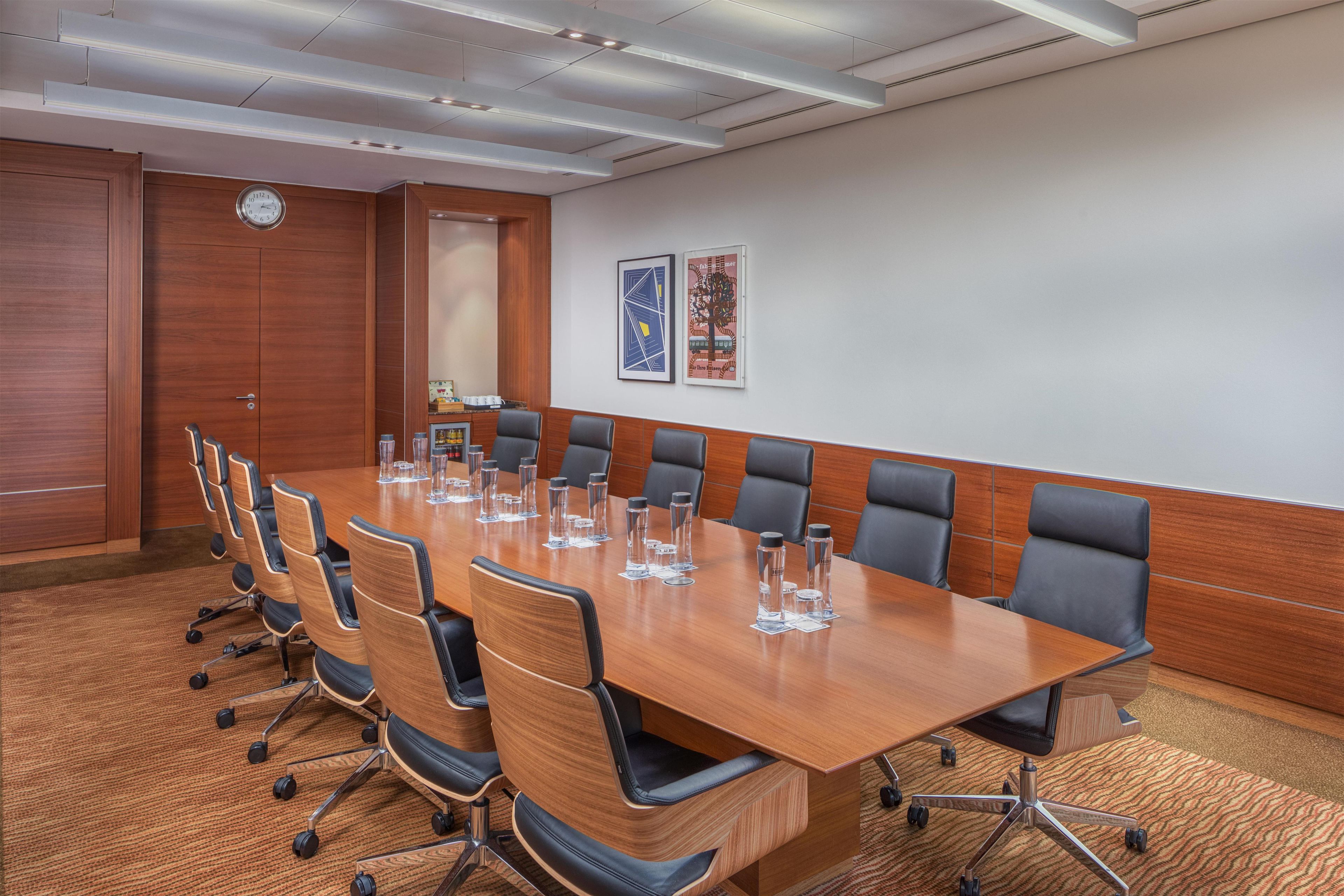 A conference room with a long table, multiple chairs, and a clock on the wall.