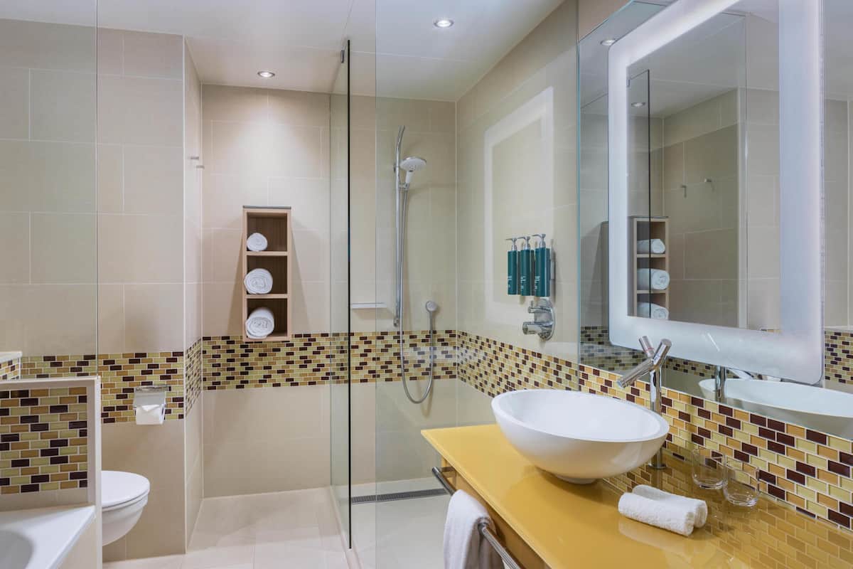 A modern bathroom with a glass-enclosed shower, a large mirror, and a beige tiled floor.