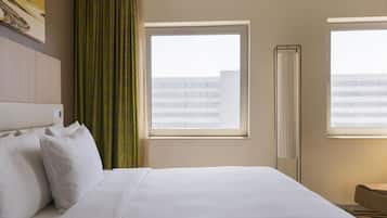 Una habitación de hotel con una cama grande, dos ventanas, un radiador y vistas a un edificio.