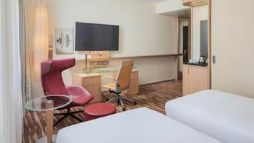 Una habitación de hotel con cama, escritorio, computadora, silla, televisor y espejo.