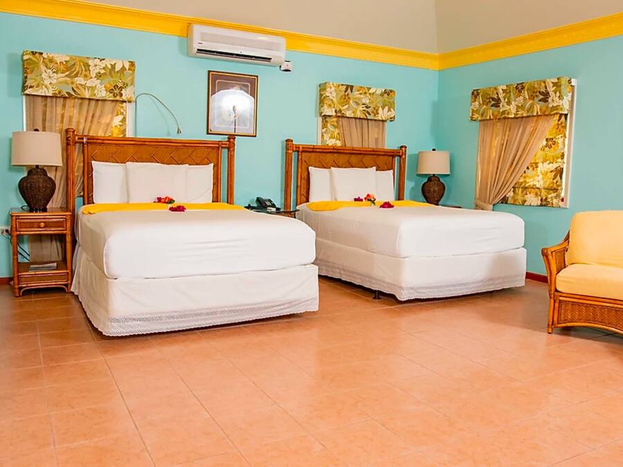 A hotel room with two beds, a chair, a nightstand, a lamp, and a picture frame.
