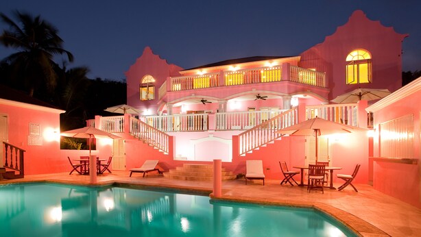 A pink building with a pool, outdoor seating, and a staircase leading to a balcony. - The Villas at Sunset Lane (St. John's)