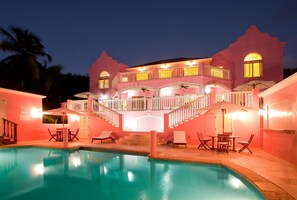 A pink building with a pool, outdoor seating, and a staircase leading to a balcony. - The Villas at Sunset Lane (St. John's)