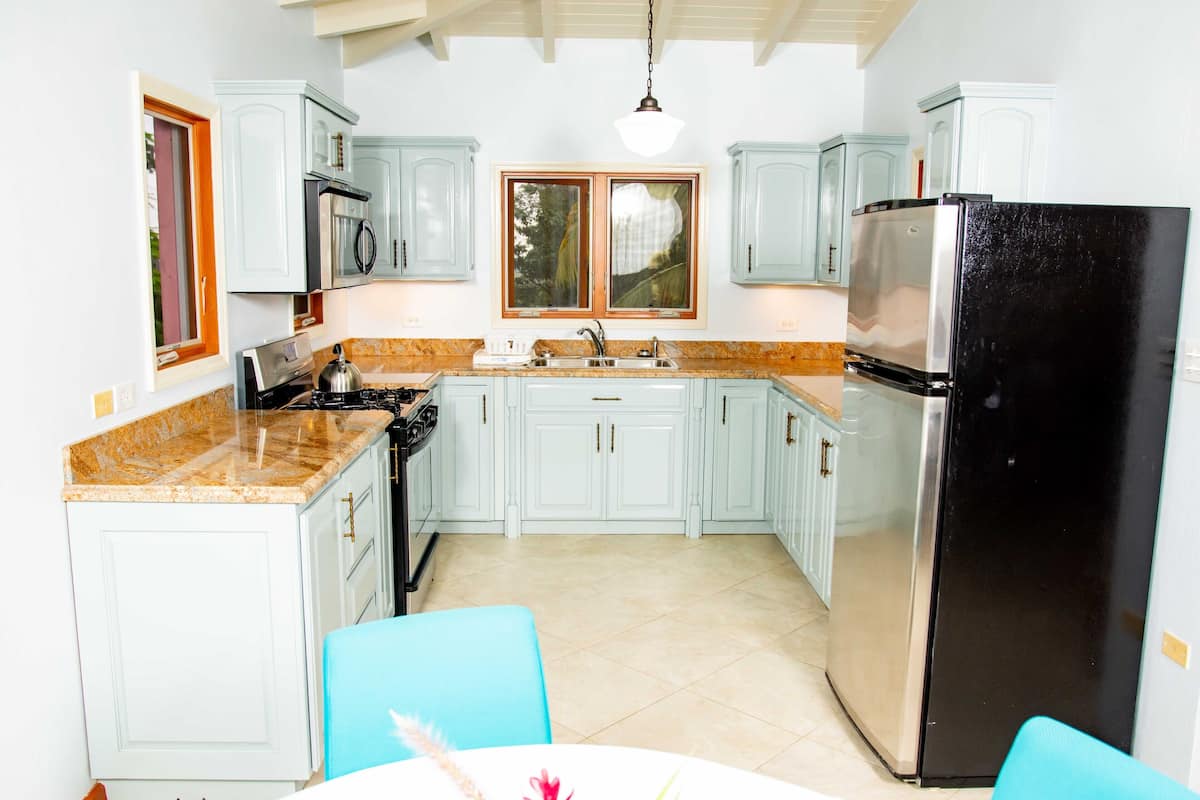 A kitchen with light blue cabinets, a black refrigerator, and a window above the sink.