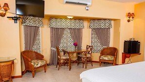 A hotel room with a bed, a TV, a dining table with chairs, and a small table with a lamp. - The Villas at Sunset Lane (St. John's)