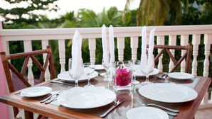 A table set for four with white plates, cutlery, and glasses, and a vase with pink flowers. - The Villas at Sunset Lane (St. John's)