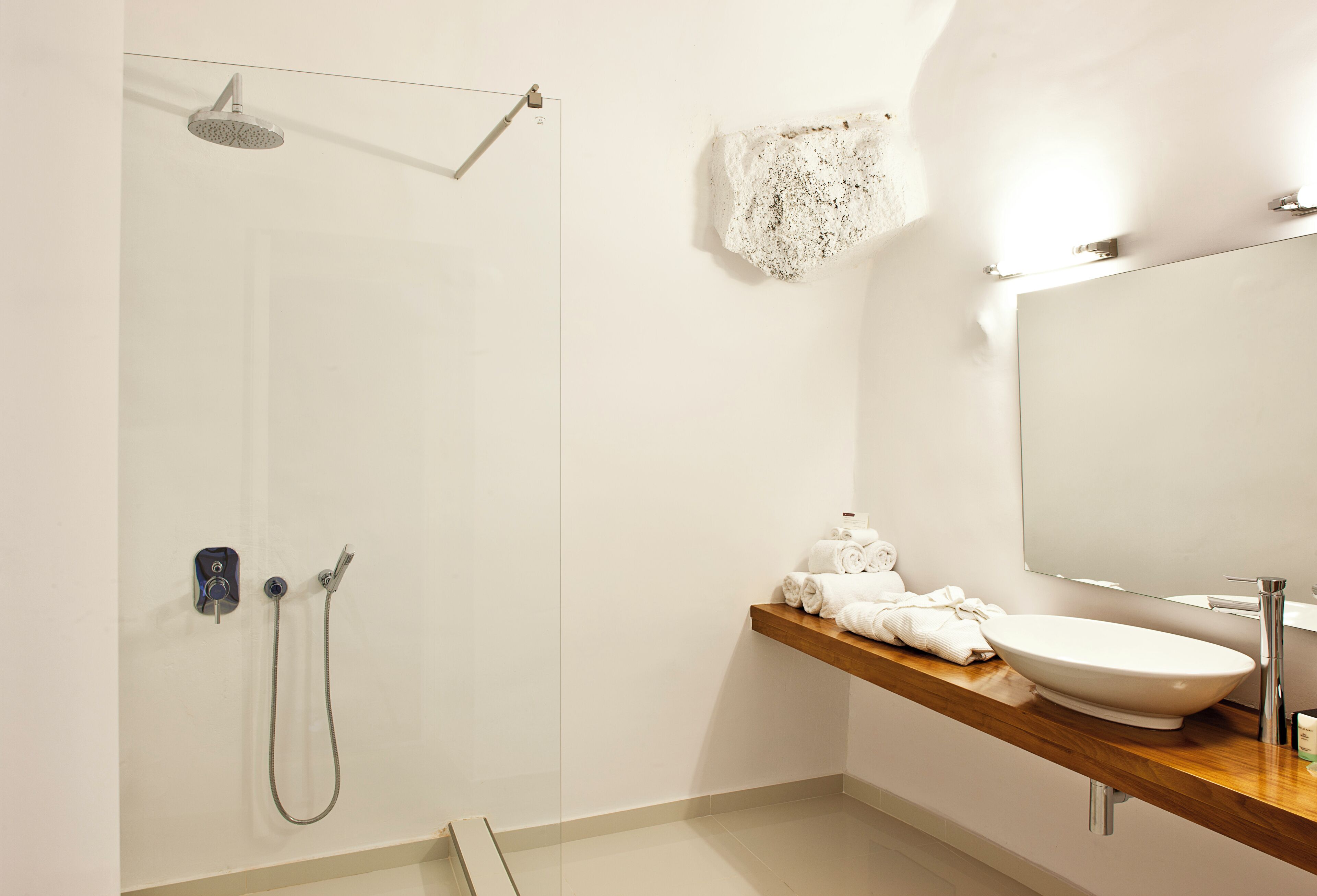 Un baño moderno con ducha, tocador de madera, lavabo y espejo.