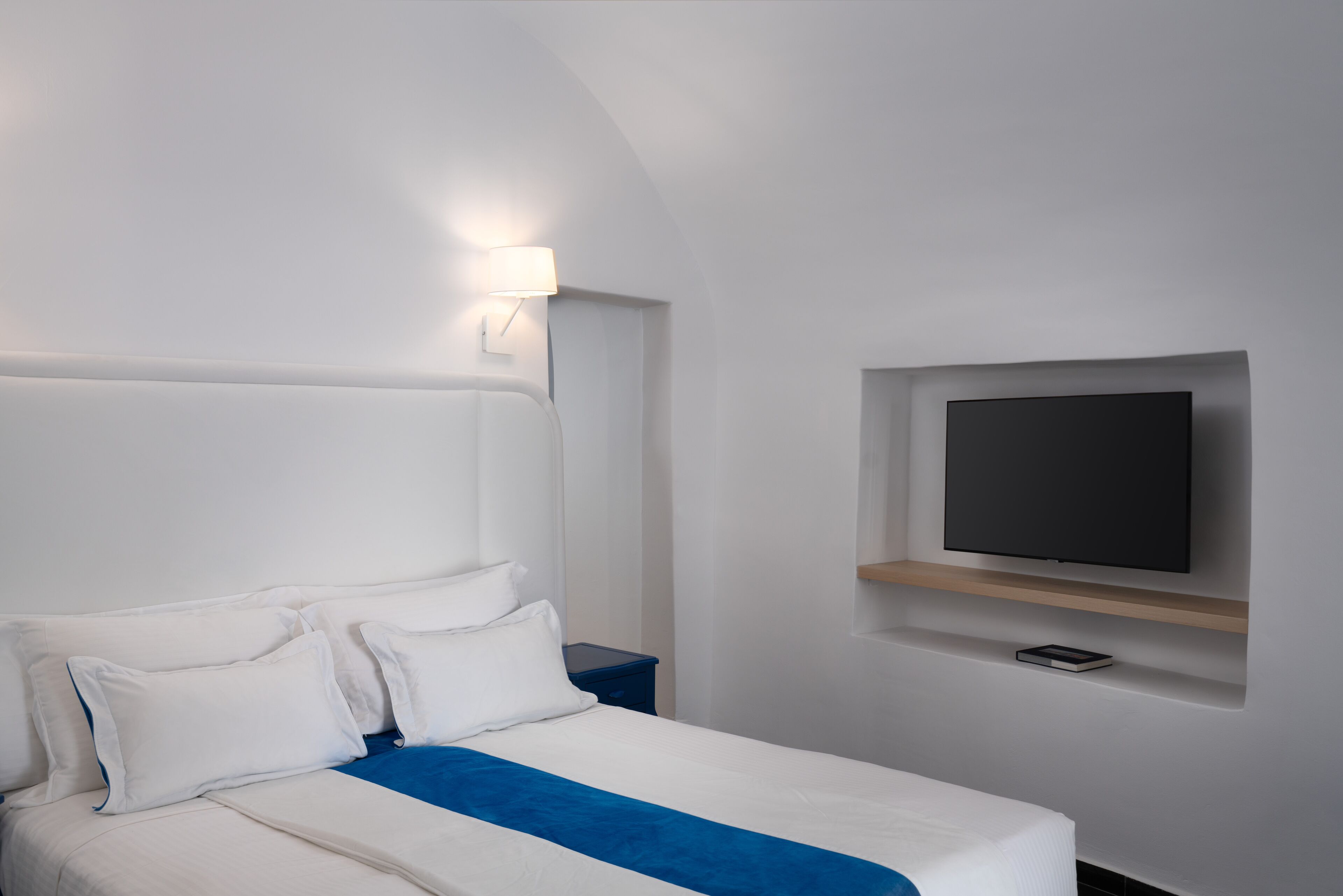 Una habitación de hotel moderna con una cama, un televisor montado en la pared y una mesita de noche.