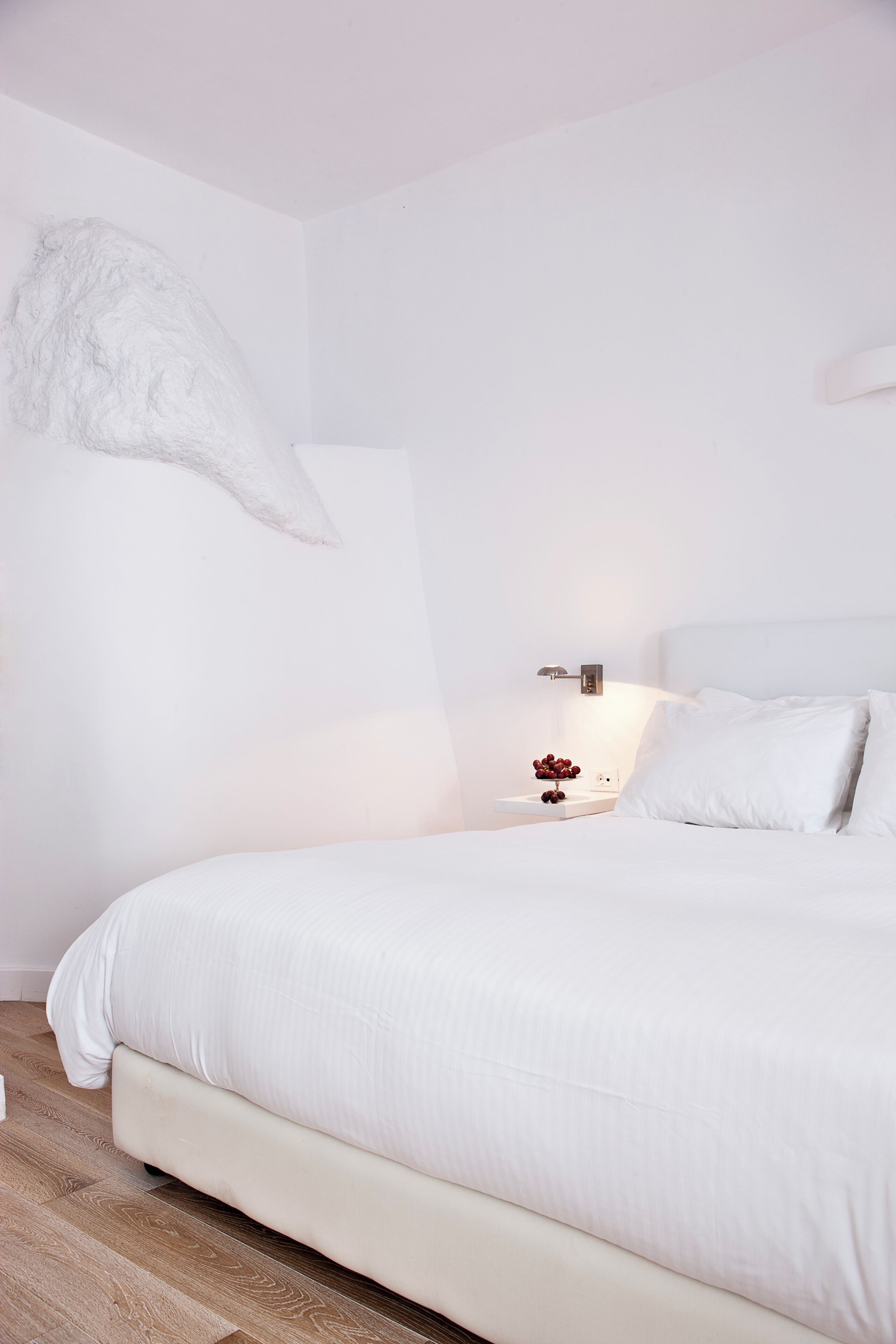 Un dormitorio minimalista con una cama grande, una mesita de noche con lámpara y una obra de arte colgada en la pared.