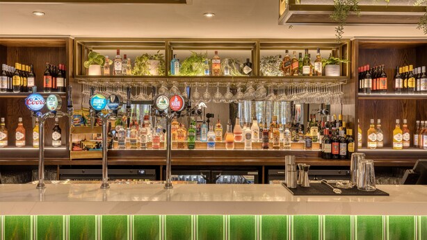 Un espace bar doté de plusieurs robinets, d’étagères remplies de bouteilles d’alcool et de verres suspendus.