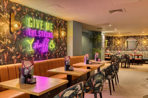 A restaurant interior with neon signage, wooden tables, and cushioned seating. - Premier Inn Birmingham Nec/Airport (Birmingham)