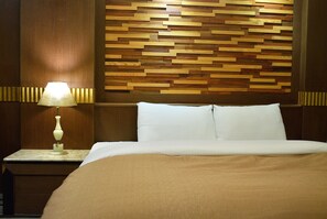 A neatly made bed with white linens and a beige throw blanket, a wooden headboard with a geometric pattern, and a bedside table with a lamp.
