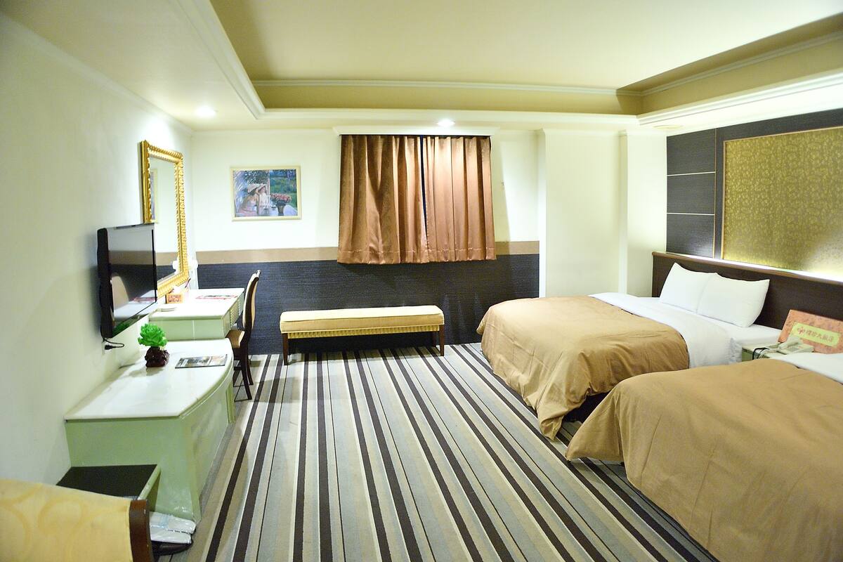 Een hotelkamer met twee bedden, een bureau met stoel, een televisie en een raam met gordijnen.