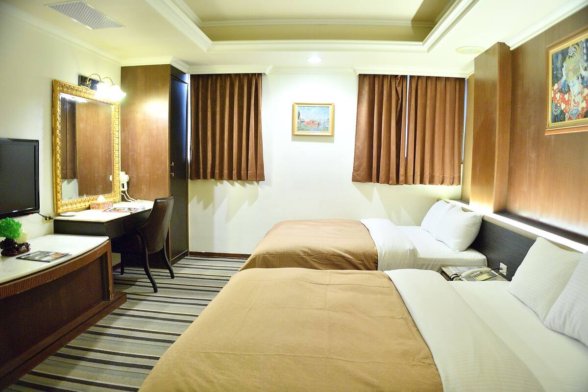 Een hotelkamer met een bureau, twee bedden, een grote spiegel en een schilderij aan de muur.