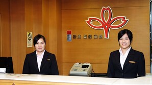 Een receptiebalie met twee receptionisten, een kassa en een muur met een logo en tekst.