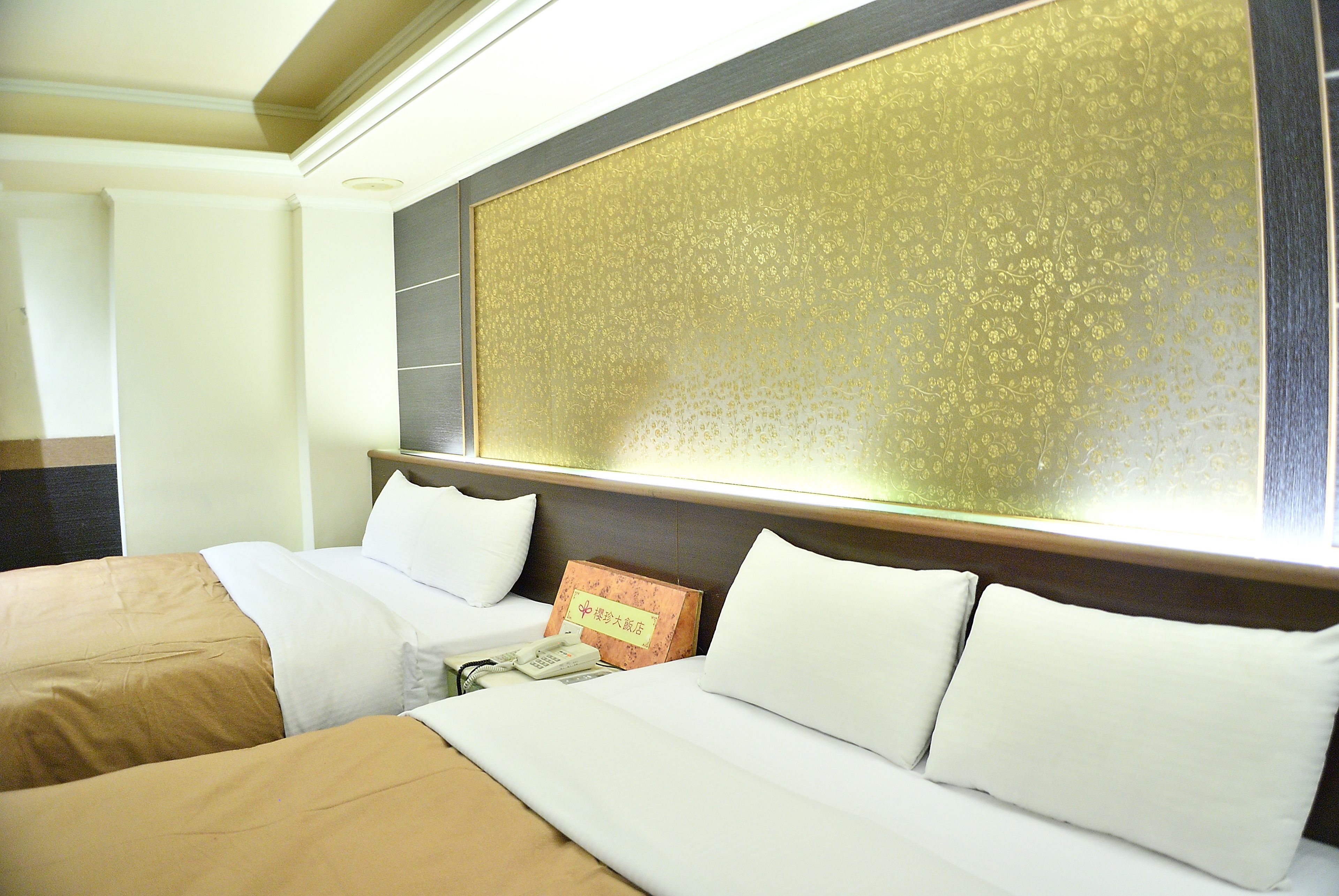 Une chambre d’hôtel avec deux lits, un grand mur orné d’un motif doré et une tête de lit en bois.