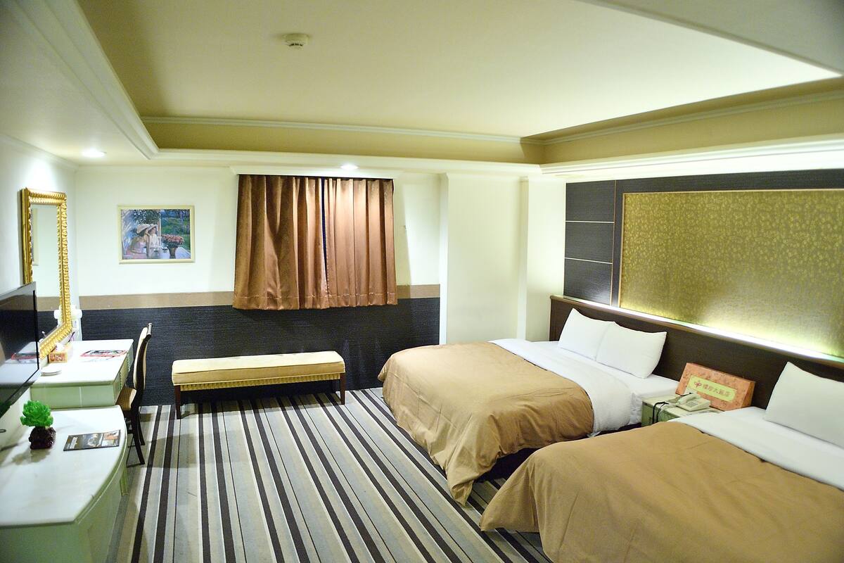 Een hotelkamer met twee bedden, een bureau, een stoel, een bankje, een spiegel en een schilderij aan de muur.