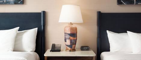 A hotel room with two beds, a nightstand with a lamp, a phone, and a clock.